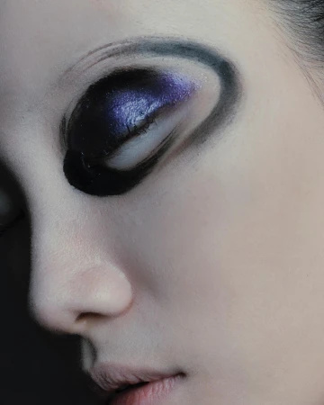 Close-up portrait of a model with artistic purple and black eyeshadow and dramatic painted eyeliner curves.