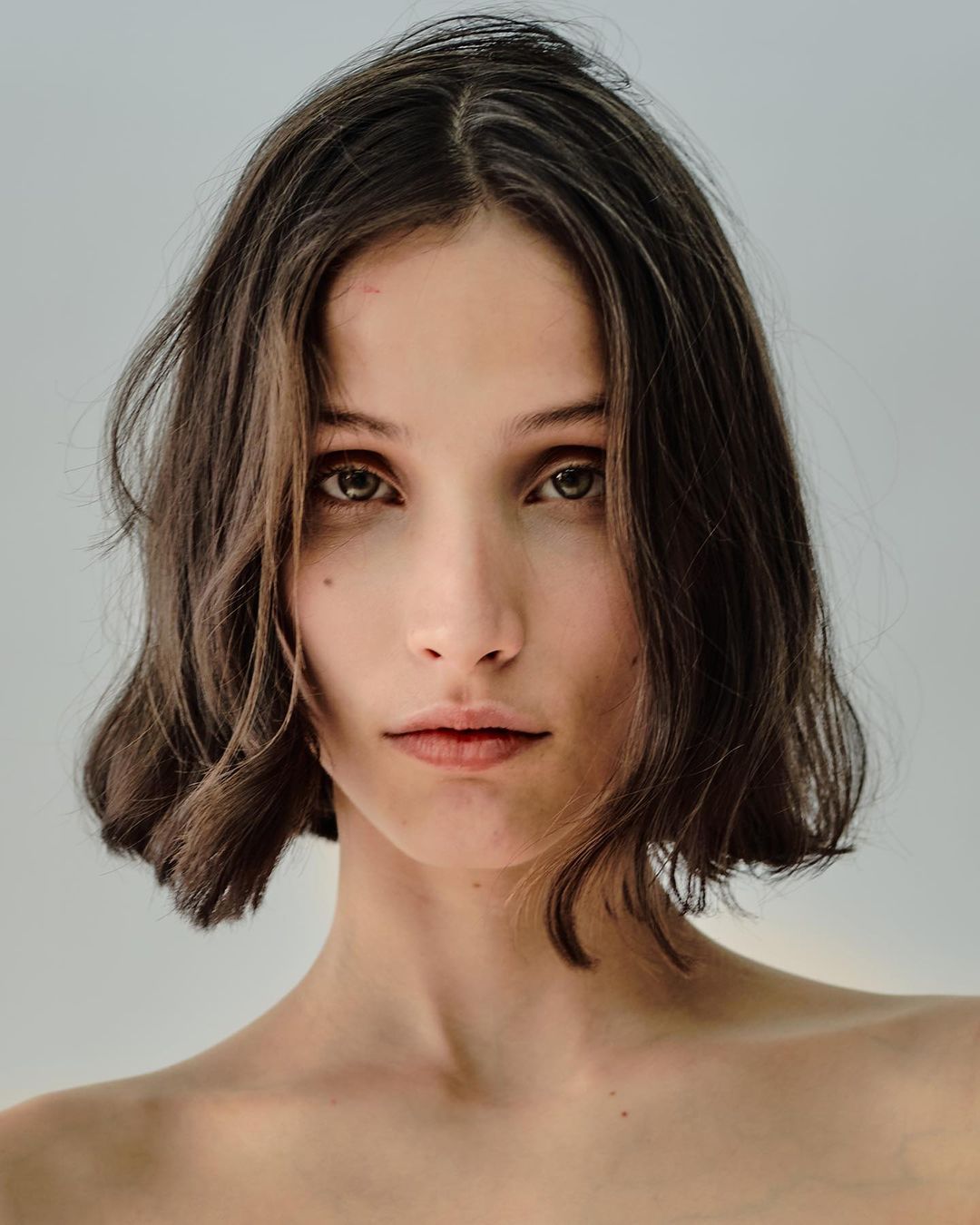 Close-up portrait of a woman with dark short bobbed hair and a neutral expression against a plain light background