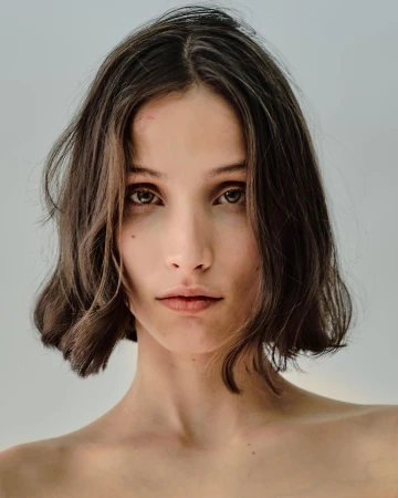 Close-up portrait of a woman with dark short bobbed hair and a neutral expression against a plain light background