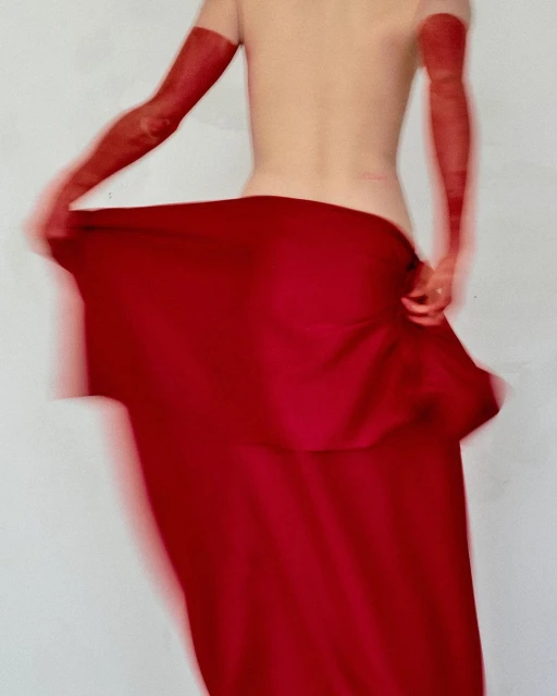 Back view of bare-backed adult with long red opera gloves and flowing red skirt in motion blur, against a plain white backdrop.