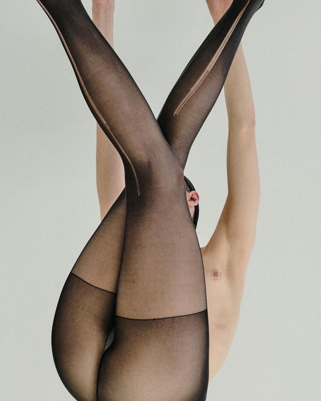 Upside-down view of adult with black tights, legs crossed, neutral background, studio lighting, fashion-inspired, artistic.