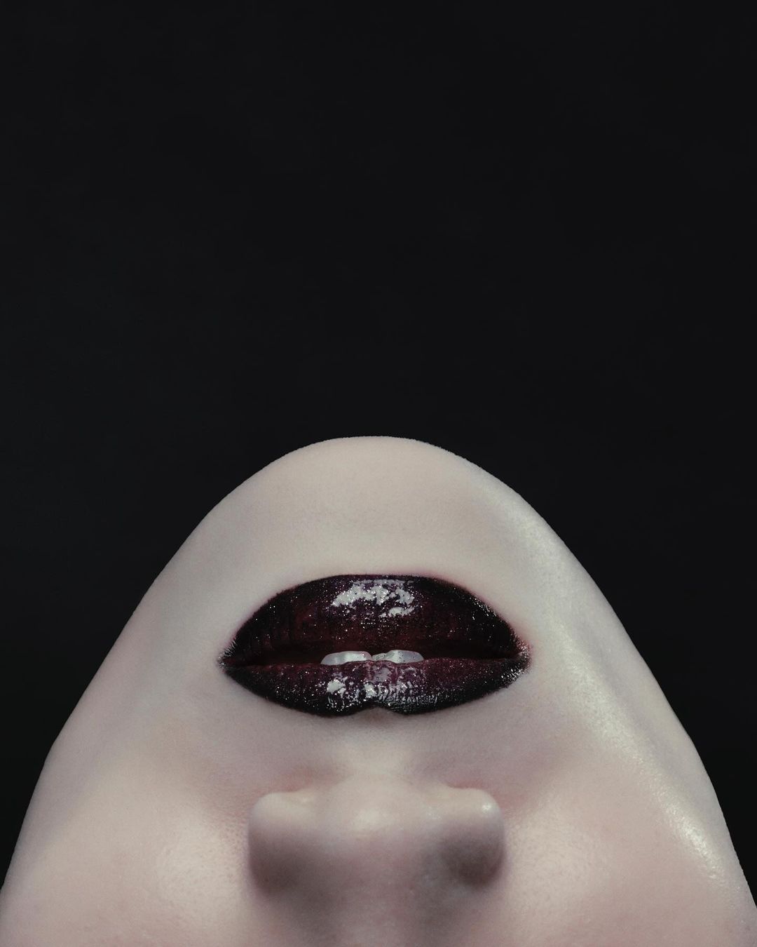 Close-up portrait focusing on dark glossy lips and chin against a solid black background by Montis Songsombat