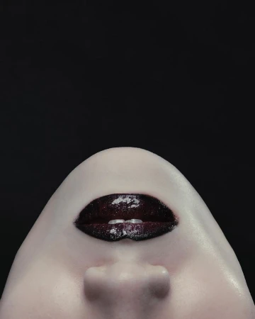 Close-up portrait focusing on dark glossy lips and chin against a solid black background by Montis Songsombat