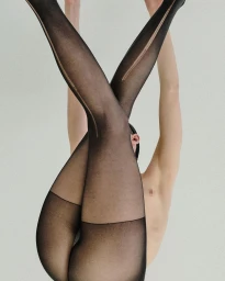 Model wearing sheer black tights with back seam lifted upside down against a plain white background