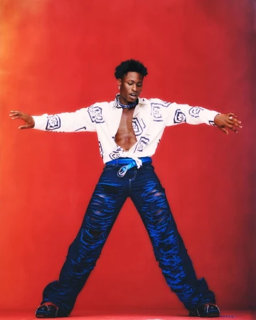 Stylish adult male with open shirt and ripped jeans poses with arms outstretched against a vibrant red studio background.