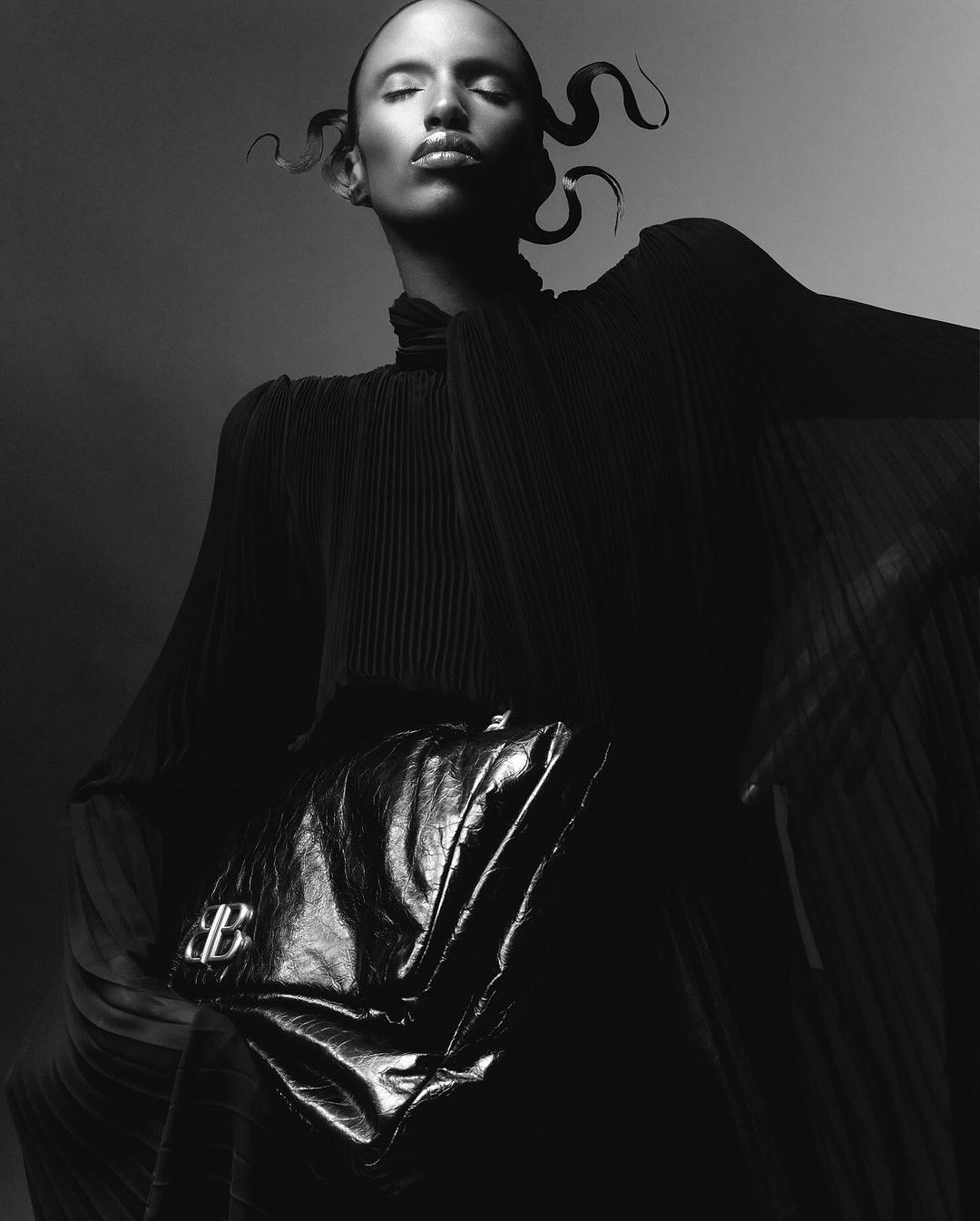 Monochrome portrait of a model with sculpted hair holding a crinkled metallic handbag in a pleated black top by Morgan Roberts