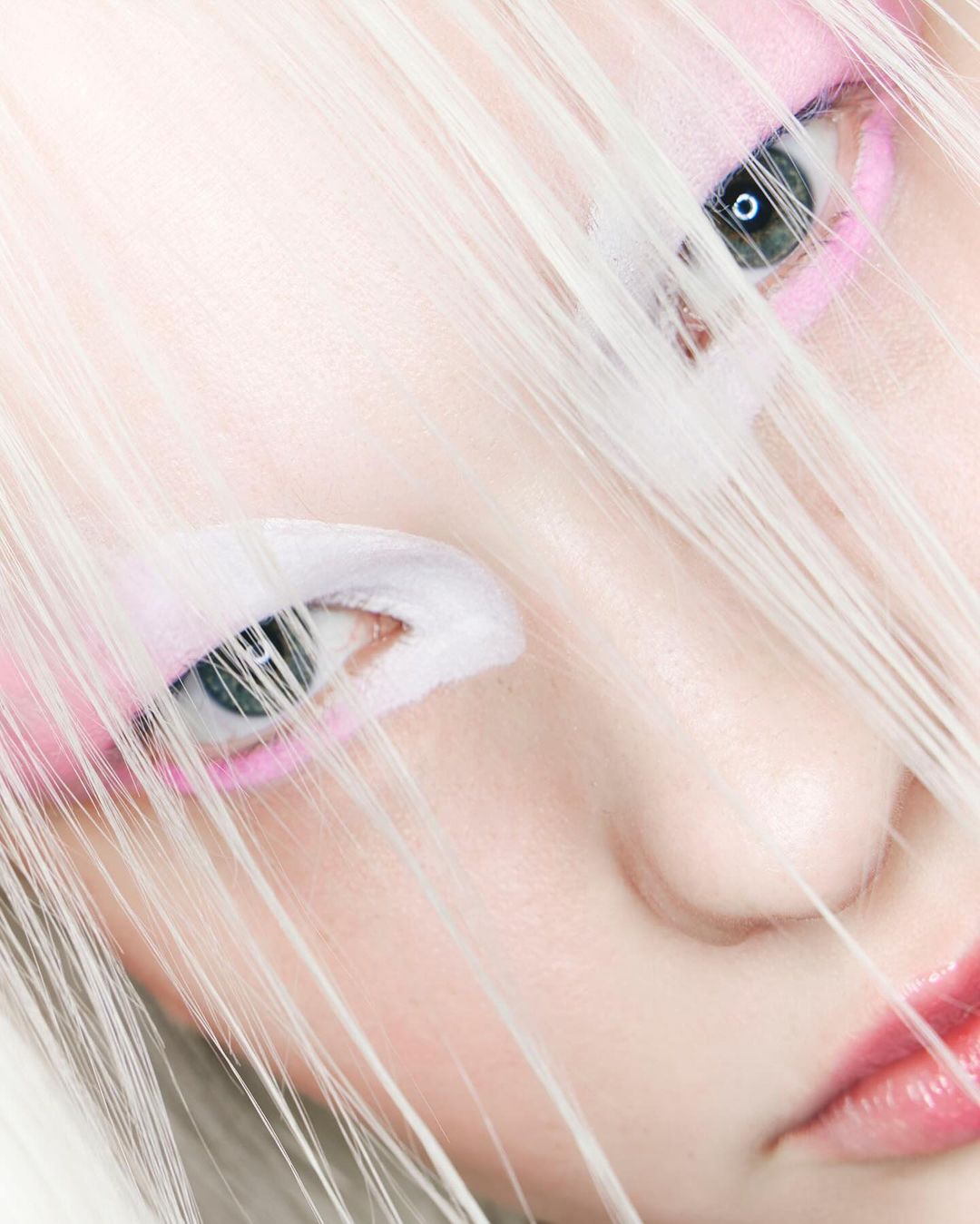 Close-up of a person with white hair and pink makeup, focusing on their eyes and facial features in a studio setting.