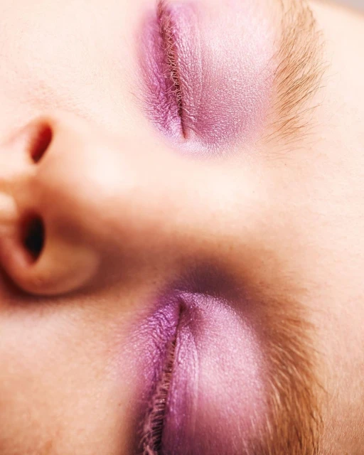 Close-up portrait of a person's face, eyes closed, featuring purple eyeshadow on the eyelids and visible facial features.
