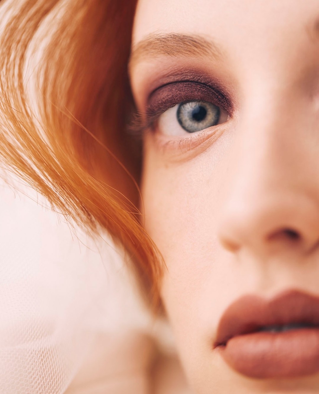 Close-up shot of a woman's face showcasing red hair, blue eye with mauve eyeshadow, and mauve lipstick, highlighting beauty and makeup.