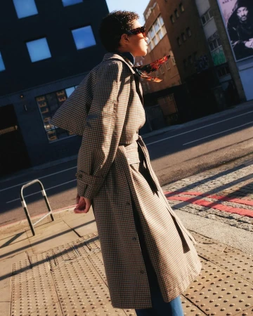 Model in houndstooth trench coat and sunglasses walking down a London street in sunlight