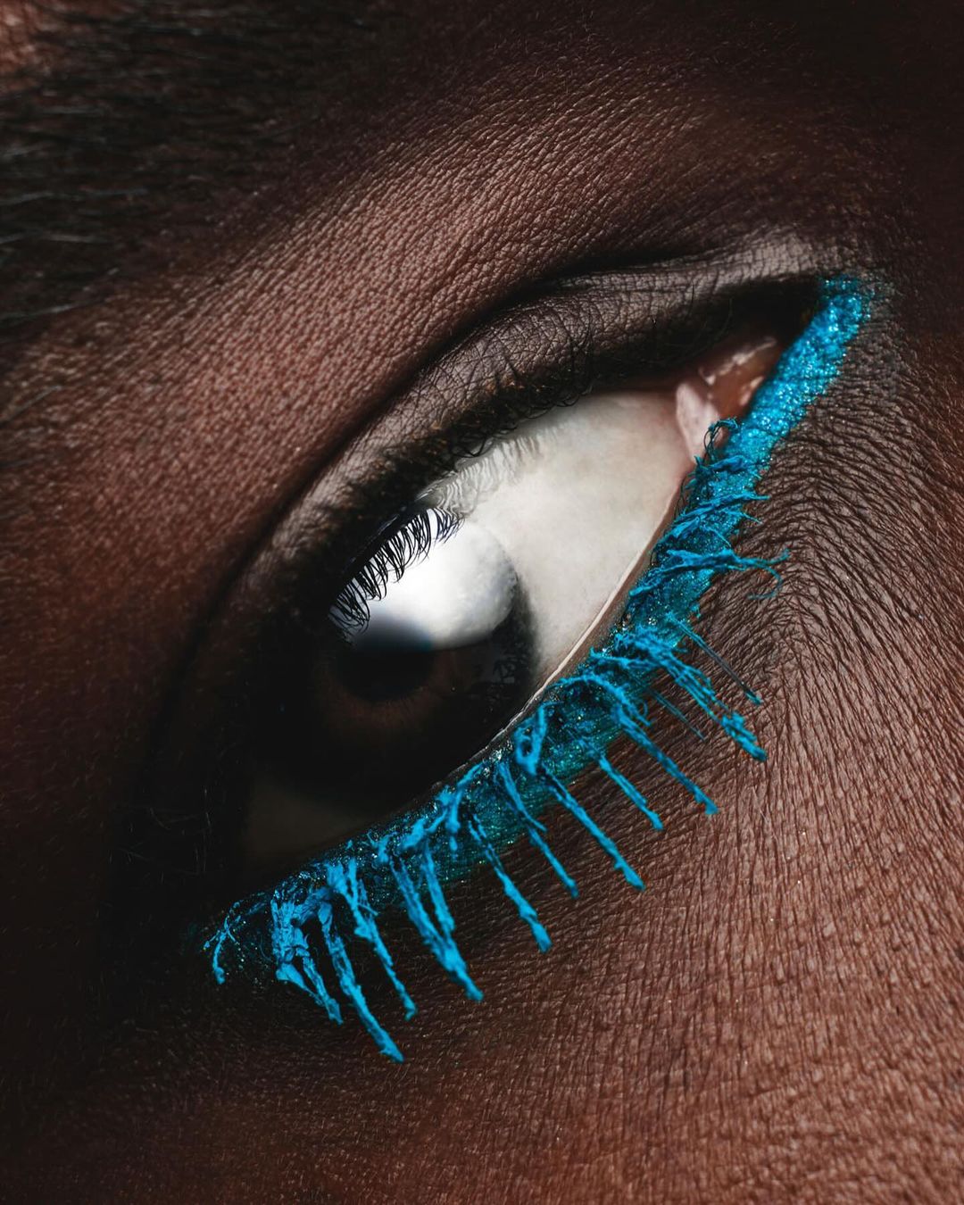 Close-up photo of a woman's eye with bright blue mascara on the lower lashes, emphasizing beauty and cosmetic artistry.