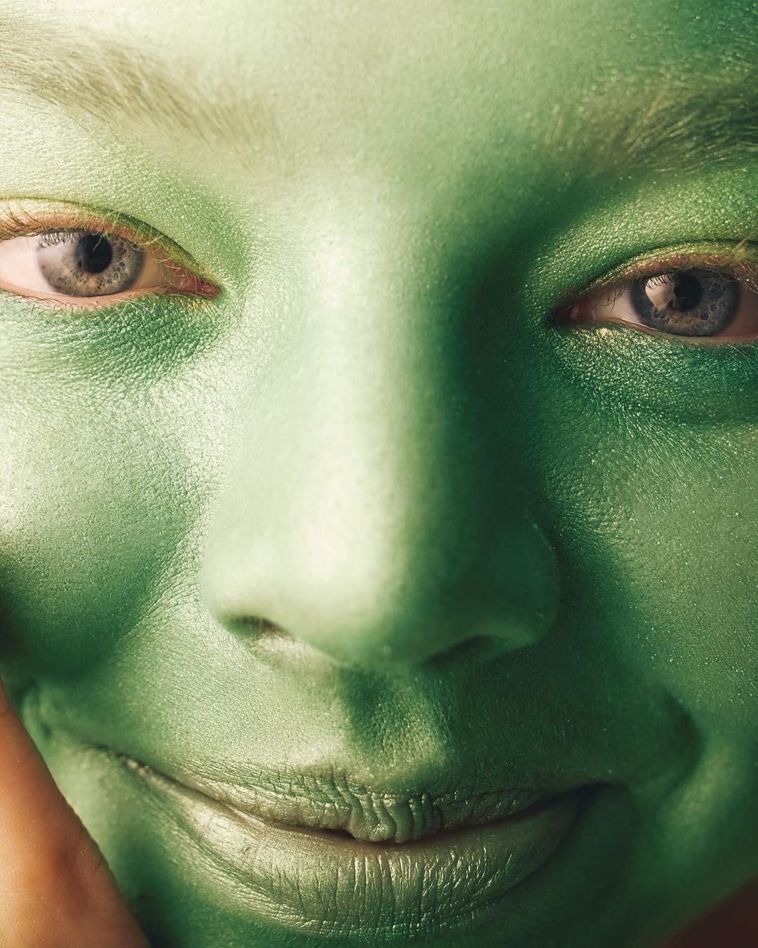 Close-up of a woman's face covered in green body paint, highlighting her eyes, nose, and lips with an overall vibrant, monochromatic effect.
