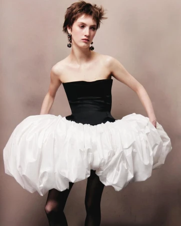 Model with short brown hair wearing a black strapless bodice and voluminous white puff skirt against a plain grey background