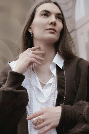 Portrait of a woman wearing a white button-down shirt, brown bomber jacket, and layered pearl necklaces by Alla Masur.