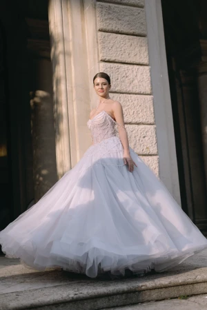 Woman in a voluminous strapless pale evening gown posing outdoors in front of classical architectural columns