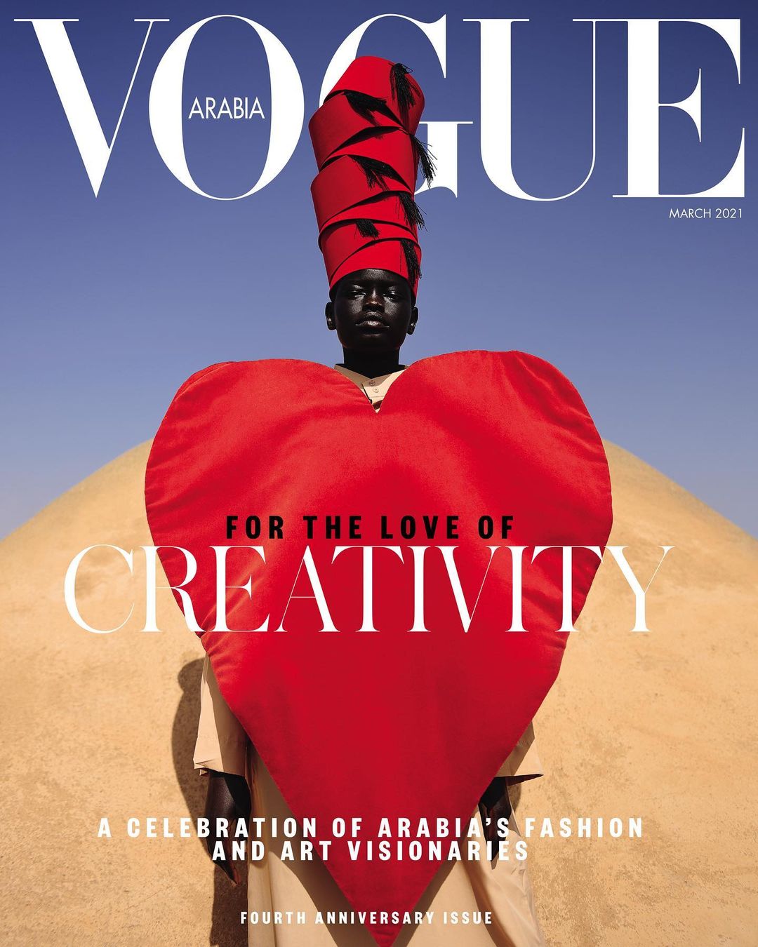 Vogue Arabia magazine cover, March 2021. A dark-skinned model in a red headdress and heart-shaped garment poses against a blue sky and desert backdrop.