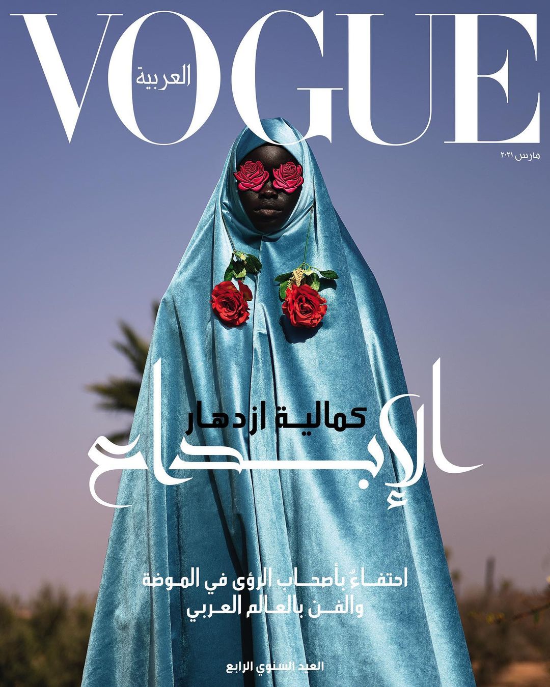 Vogue Arabia cover featuring a Black woman in a light blue robe adorned with red roses, set against a clear blue sky backdrop.