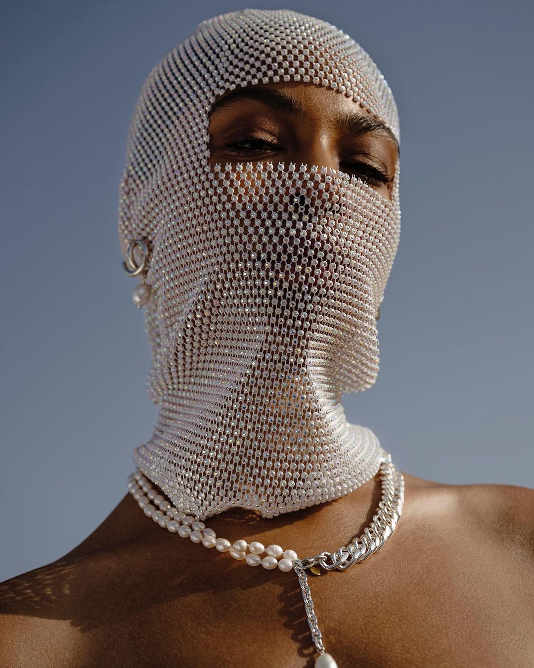 Person wearing a beaded head covering and pearl necklace against a blue sky, creating a striking and fashionable portrait.