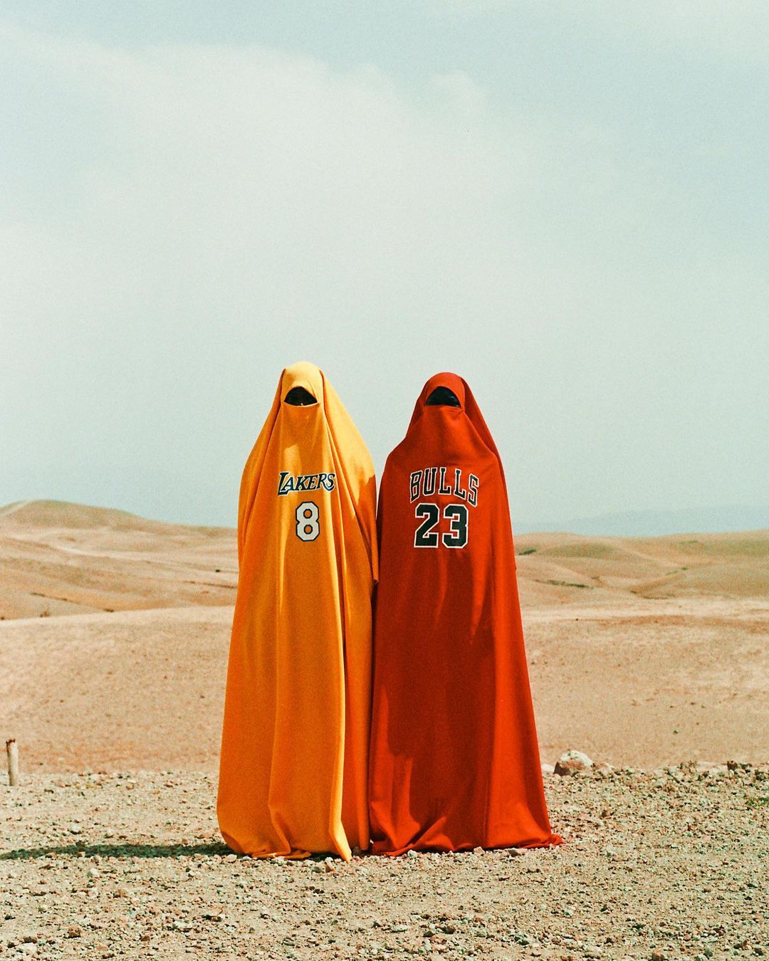 Two figures in NBA jerseys stand in a desert landscape; one in a Lakers jersey and one in a Bulls jersey.