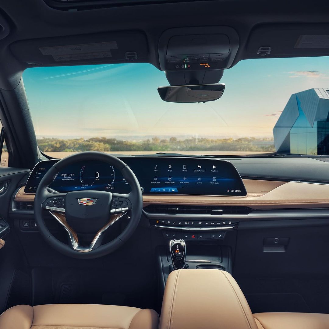 Cadillac LYRIQ dashboard features a digital display and steering wheel, showcasing the car's interior design with a view of a modern building.