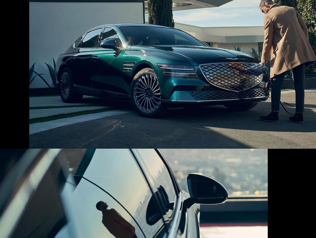 A dark green Genesis electric car is charging, a man plugs in the charger in a modern architectural setting with natural light.