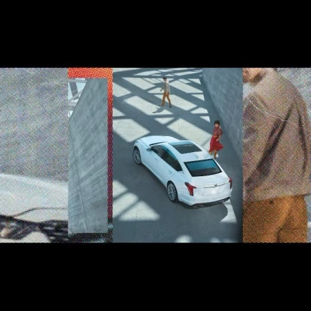 High-angle shot of a white Cadillac CT5 parked in an urban environment, with two people walking nearby. The car and environment are modern.