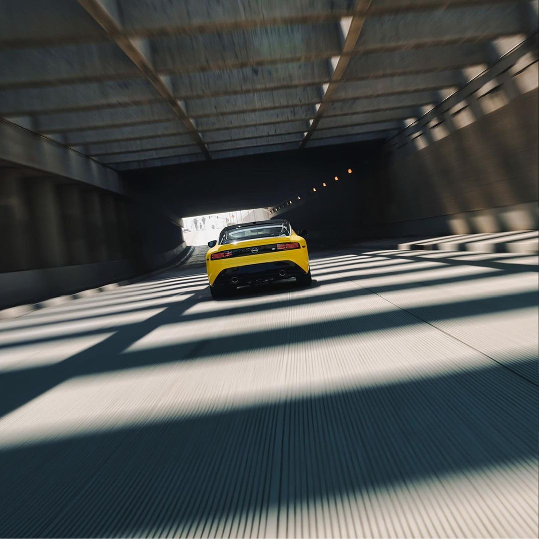 Yellow convertible car driving through a concrete tunnel with bright light at the exit, creating dynamic shadows and emphasizing speed.