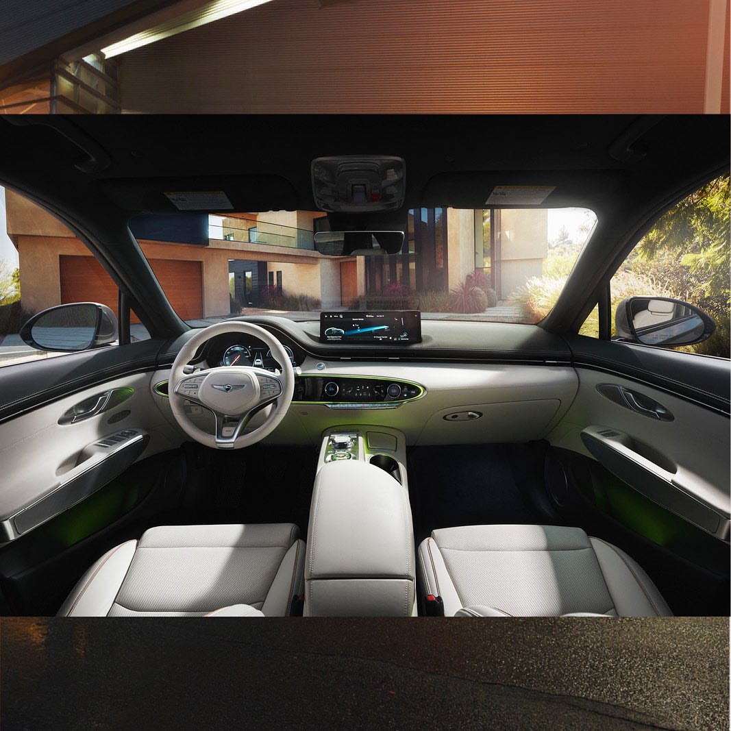 Car interior shot featuring a white and grey color scheme, showcasing the dashboard, seats, and center console, with a home exterior visible.