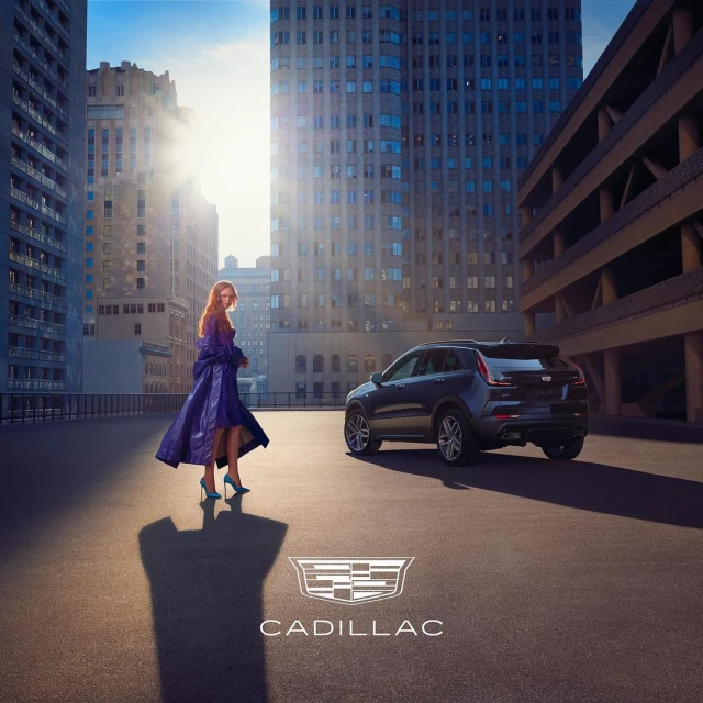 A woman stands near a black Cadillac SUV against an urban backdrop with skyscrapers, showcasing fashion and automotive elements.