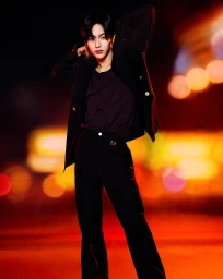 Portrait of a man in black blazer and dark trousers posing against an out-of-focus background with warm bokeh lights by Munachi Osegbu.