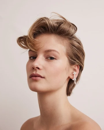 Close-up portrait of a woman with short blonde hair and a silver ear cuff against a plain light background