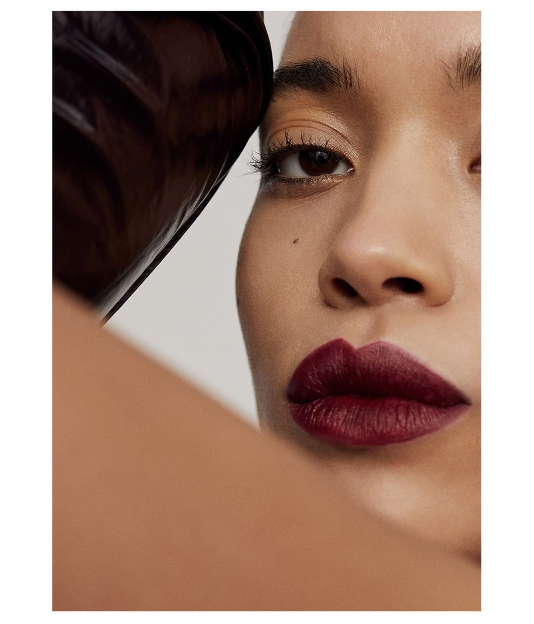 Close-up shot of an adult woman with dark burgundy lipstick, fair skin tone, and light eye makeup on a neutral grey background.