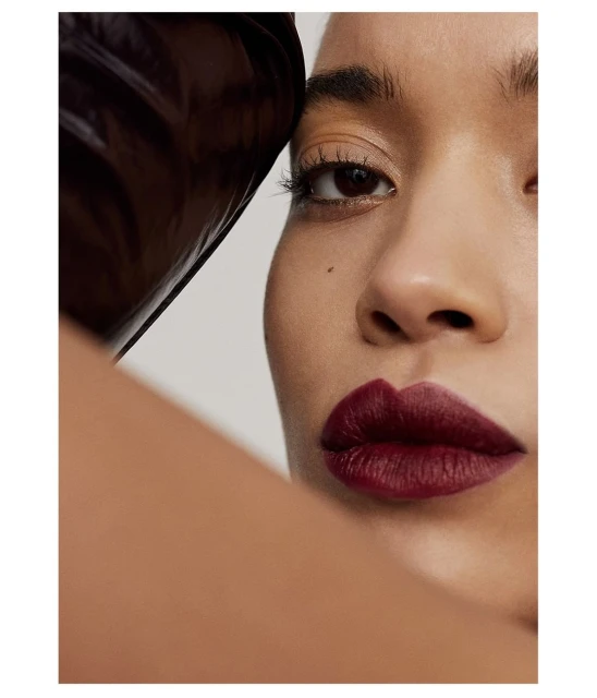 Close-up shot of an adult woman with dark burgundy lipstick, fair skin tone, and light eye makeup on a neutral grey background.