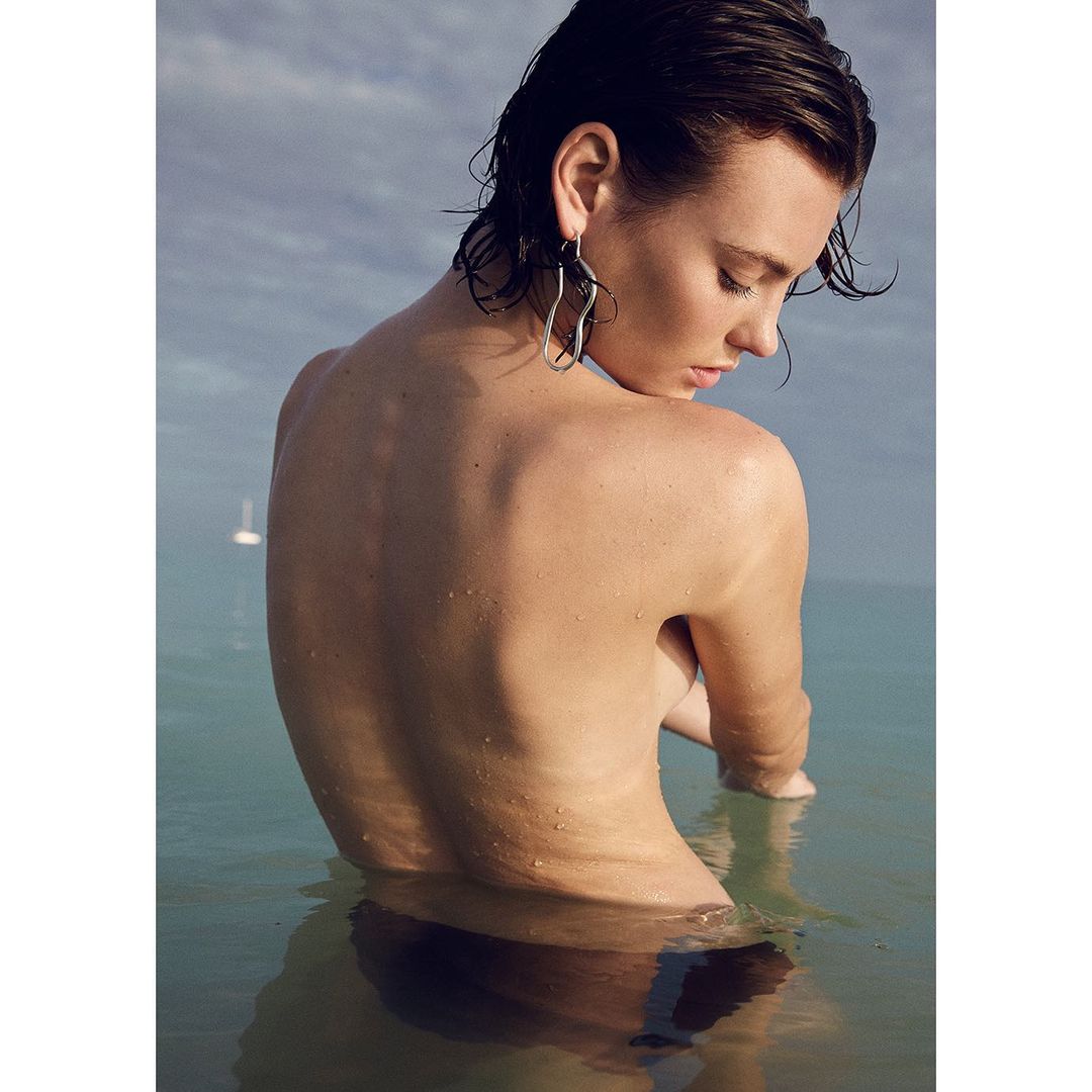 Woman with wet hair wearing a silver earring standing in the ocean under an overcast sky, photographed in Paris by Muriel Liebmann.