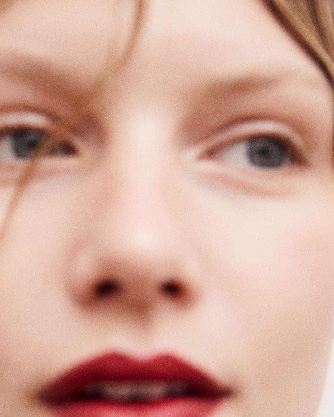 Extreme close-up of a woman's face with focus on her eyes, nose, and red lips, creating a beauty and fashion portrait.