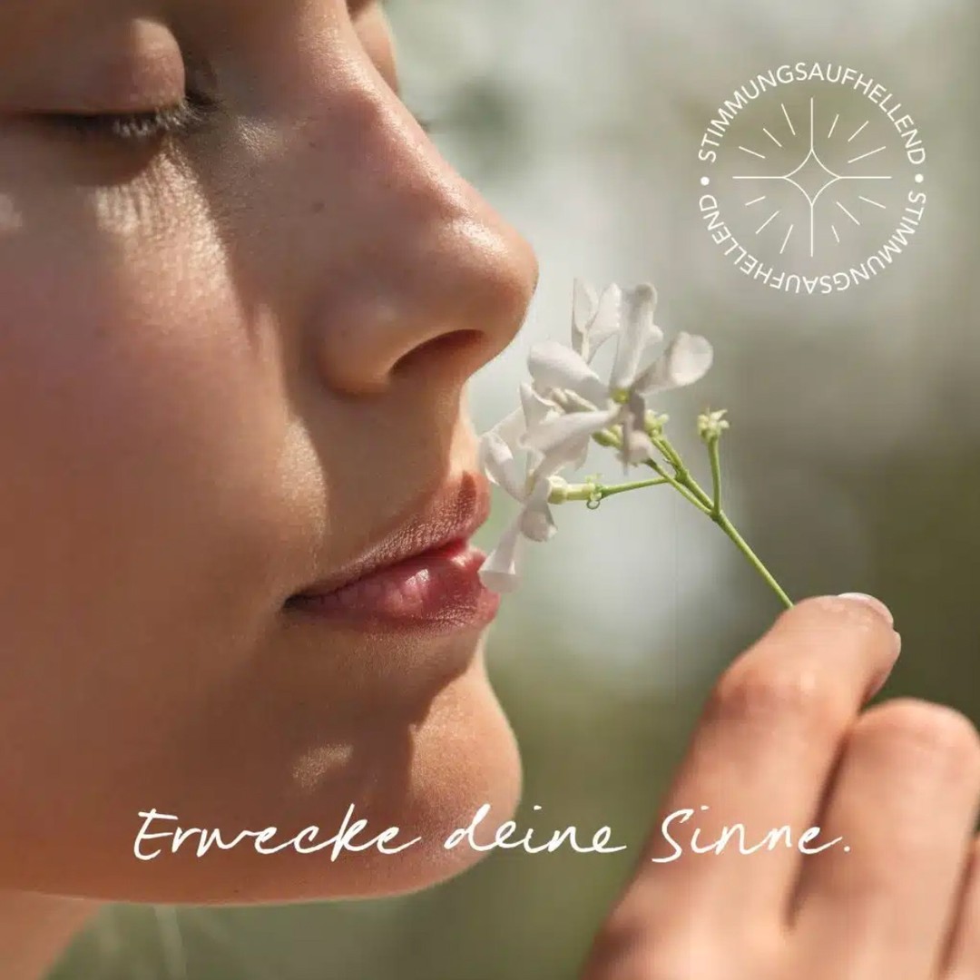 Close-up of an adult female face in profile, eyes closed, smelling small white flowers, creating a serene, natural, and beauty-focused image.