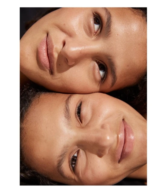 Close-up of two adult women with warm skin tones lying head-to-head, smiling gently with soft lighting, and smooth skin.