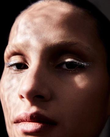 Close-up portrait of a woman's face with dramatic lighting, showcasing her features and makeup, set against a dark background.