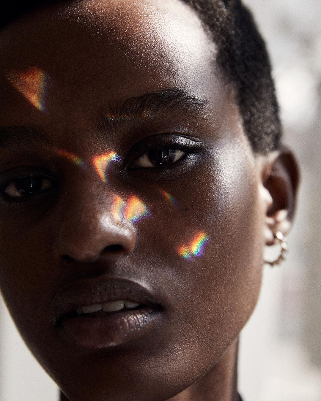 Close-up portrait of a Black female adult with short hair, light reflecting on her face, and wearing hoop earrings against a blurred background.