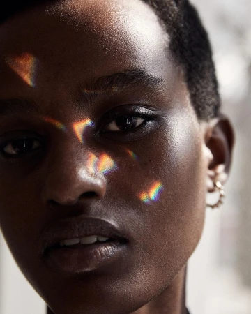 Close-up portrait of a Black female adult with short hair, light reflecting on her face, and wearing hoop earrings against a blurred background.