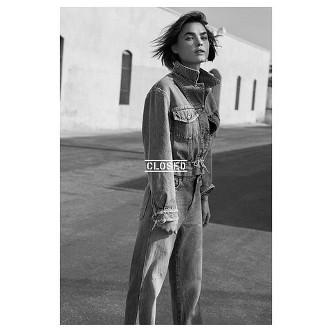 Monochrome fashion shot of a woman in a denim jumpsuit posing outdoors against a bright building on a sunny day.