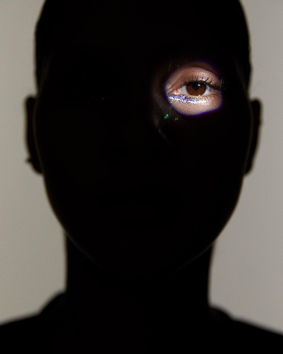 Dramatic beauty portrait: Woman's eye with glitter makeup is highlighted against dark shadows, creating high contrast.