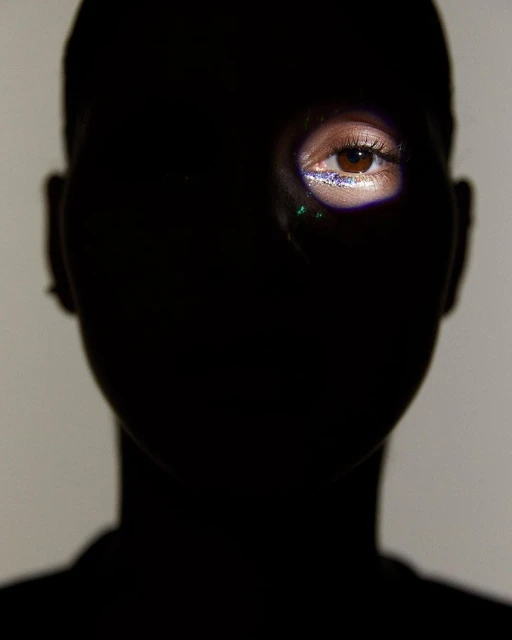 Dramatic beauty portrait: Woman's eye with glitter makeup is highlighted against dark shadows, creating high contrast.