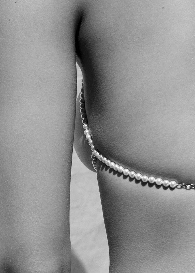 Close-up studio shot: An adult poses with pearl body jewelry, emphasizing skin texture, monotone color grading and minimalist aesthetic.