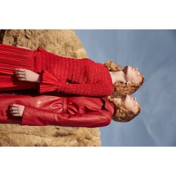 Two red-haired models in vibrant red outfits posing against a rocky landscape under a blue sky, photographed by Muriel Liebmann.