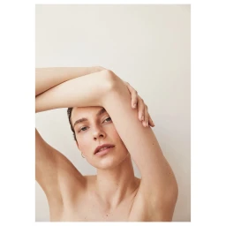 Close-up portrait of a woman with arms raised framing her face against a plain light background