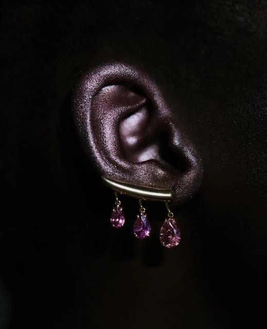 Close-up shot of a human ear adorned with dangling pink gemstone earrings, set against a deep black background, showcasing beauty and jewelry.