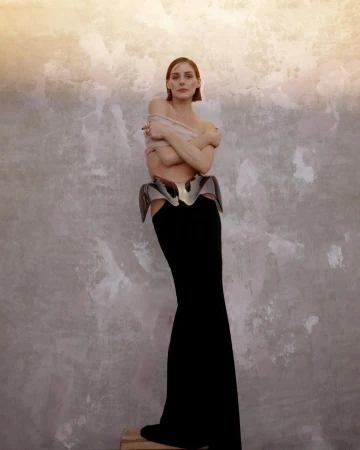 Woman in a black maxi skirt and metallic peplum corset standing against a mottled textured wall.