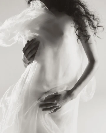 Model draped in sheer white fabric with long curly hair captured in a moody monochrome portrait by Myrthe Giesbers.