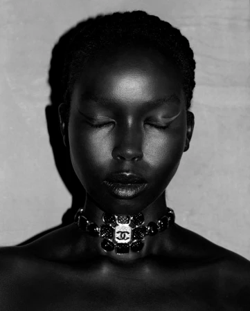 Close-up portrait of a black woman with closed eyes wearing a statement choker necklace, shot in high-contrast monochrome.